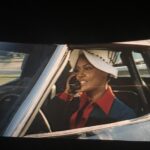 A woman sitting in a car on a big screen.