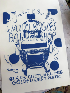 A blue and white poster features a barber chair, clippers, and a comb with text: "Waldo Bogges Barber Shop, Black Cultural Hub, Golden West Hotel, Est. 1913.