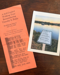 Two items: an orange pamphlet about a walking tour on Timothy S. Pettis’s 1924 death, and a photo of a memorial sign by a calm waterfront at sunset.